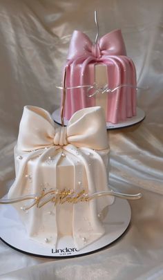 two cakes decorated with bows and ribbons are on white plates, one is pink and the other is gold