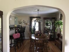 an archway leads into a dining room and kitchen area with hardwood floors, white walls, and wooden furniture