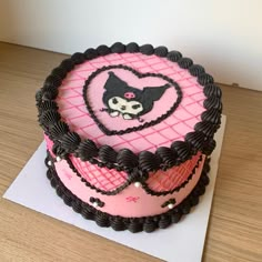 a pink and black cake on top of a wooden table next to a white paper