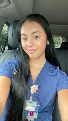 a woman sitting in the back seat of a car with long black hair and wearing a blue scrub top