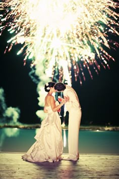 two brides standing on a dock with fireworks in the background