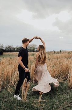 a man and woman dancing in the middle of a field with tall grass behind them