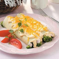 a white plate topped with broccoli and cheese covered burrito next to a tomato