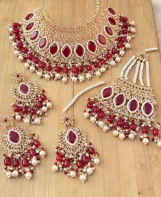 a necklace and earring set with red stones, white pearls and gold chains on a wooden surface