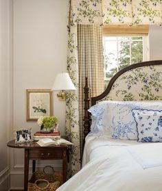 a bed sitting next to a window in a room with floral wall paper on the walls