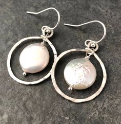 There is a reason why classic style is classic style, and you just can't go wrong with pearls. These earrings feature gorgeous 11mm coin pearls framed by hammered sterling silver circles, and finished with a simple ear wire. These pearls are a contemporary shape, and have a wonderful white to cream color and a great luster. Please note that while I select the best pearls available, freshwater pearls are a natural material and often have some minor imperfections. All items are packaged in a gift Elegant Circle Pearl Jewelry, Elegant Pearl Circle Jewelry, Elegant Circular Pearl Jewelry, Elegant Pearl Jewelry In Circle Shape, Pearl White Sterling Silver Round Pearl Earrings, Pearl White Round Sterling Silver Pearl Earrings, White Sterling Silver Small Hoop Earrings, Elegant Dangle Hoop Earrings For Mother's Day, Small Hoop White Sterling Silver Jewelry