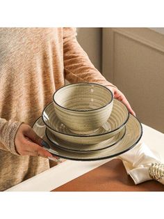 a woman holding a stack of plates on top of a counter