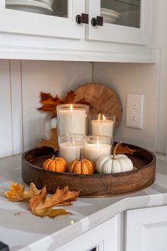 candles are sitting in a wooden tray on a counter top with autumn leaves and pumpkins