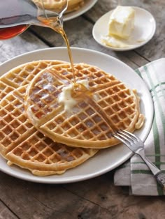 two waffles on a white plate with syrup being poured over them and butter