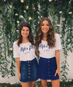 two young women standing next to each other in front of a wall with white flowers