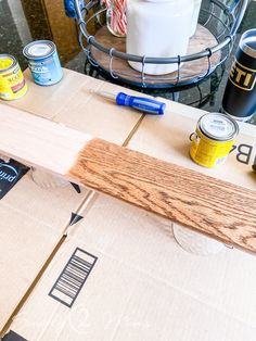 the contents of a wooden table with paint and wood planks on it in front of a wire basket