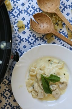 a white plate topped with pasta next to wooden spoons on a blue and white table cloth