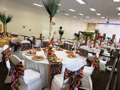 a banquet hall decorated with white tables and colorful sashes, palm trees and other decorations