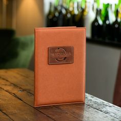 an orange leather book sitting on top of a wooden table next to bottles of wine