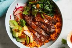 a white bowl filled with meat and vegetables next to a cup of sauce on a table