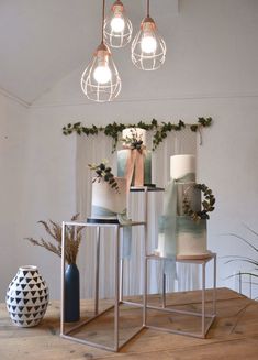 three different types of cakes on display in a room with plants and lights hanging from the ceiling