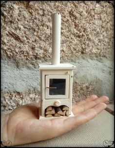 a hand holding an old fashioned stove in front of a wall with wood chips on it