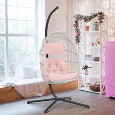 a white swing chair with pink cushions in a bedroom