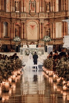 a bride and groom standing at the alter in front of an ornate church with candles