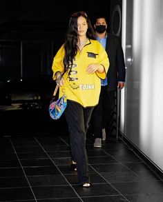 a woman in a yellow shirt and black pants is walking down the street with her handbag