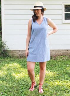 a woman standing in the grass with her hands on her hips and wearing a hat