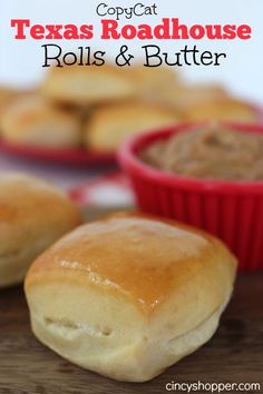 rolls and butter sitting on top of a wooden table next to red bowls filled with food