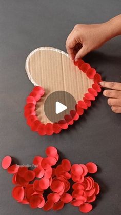 someone is making a heart out of paper and some red circles on the table next to it