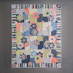 a patchwork quilt hanging on the wall in front of a gray wall with an orange, blue and green flowered design