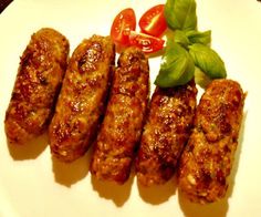 several sausages on a white plate with tomatoes and basil garnished in sauce