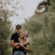 a man and woman hugging each other in the woods