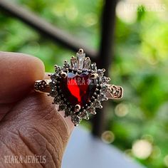 a person holding a ring with a heart shaped stone in the middle and surrounded by diamonds