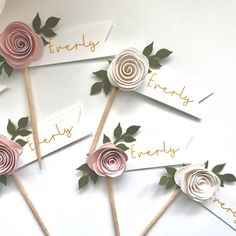 four paper flowers are arranged on sticks with name tags attached to them, and the stems have green leaves