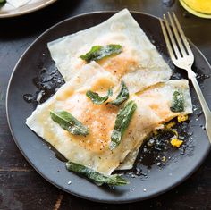 a black plate topped with ravioli covered in cheese and green leafy toppings