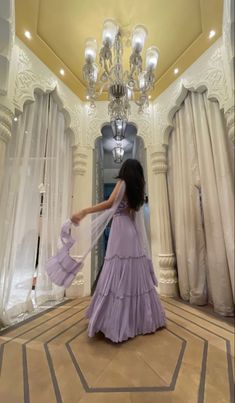 a woman in a long purple dress is walking through a room with chandelier