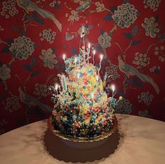 a multicolored cake sitting on top of a table with lit candles in it