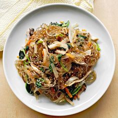 a white plate topped with noodles and veggies on top of a wooden table