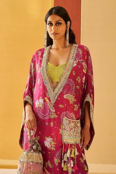 Majenta pheran kaftan with all over floral print, highlighted with zardozi, sequins and jute. Paired with a coordinating floral print joggers and lime green bustier
Components: 3
Pattern: Embroidery, Print
Type Of Work: Zardozi, Sequins, Jute, Floral
Neckline: Deep V Neck
Sleeve Type: Flared Sleeves
Fabric: Silk, Lurex
Color: Pink
Other Details: 
Zardozi embroidered patch-pocket with tassels
Note:
Potli bag held by the model is not for sale
The pink outfit worn by the other model is not for sale Festive V-neck Kaftan With Floral Print, Festive Floral Print Maxi Kaftan, Designer Kaftan With Printed Motifs For Eid, Designer Wear Printed Kaftan For Eid, Bollywood Style Kaftan With Printed Motifs For Eid, Designer Eid Kaftan With Printed Motifs, Eid Bollywood Kaftan With Printed Motifs, Festive Designer Kaftan With Printed Motifs, Bollywood Silk Kaftan With Printed Motifs