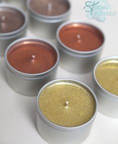 four tins filled with different colored candles on a white counter top next to each other