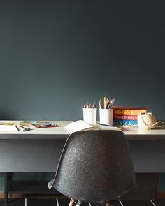 a desk with a chair and books on it in front of a wall that has been painted dark green