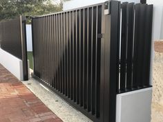 a black gate that is on the side of a building next to a brick walkway