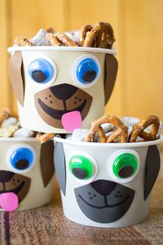 three paper cups with dog faces and pretzels in them