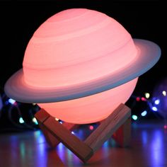 an illuminated saturn lamp sitting on top of a wooden stand in front of some lights