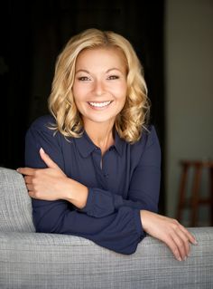 a woman sitting on top of a gray couch smiling at the camera with her arms crossed