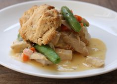 a white plate topped with meat and veggies covered in gravy on top of a wooden table