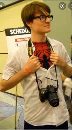 a young man holding a camera and looking at the spiderman shirt on his chest