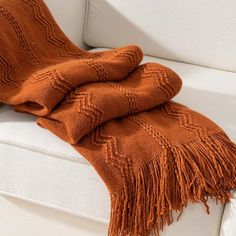 an orange blanket sitting on top of a couch next to a white sofa cushion and pillow