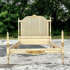 an old fashioned bed frame in the middle of a parking lot with trees in the background