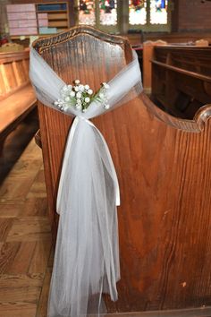 a white ribbon tied to the back of a wooden church pew with flowers on it