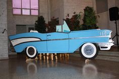 an old fashioned blue car sitting on top of a wooden table in a room filled with windows