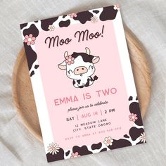 a pink and black cow birthday party card on a wooden platter with white linens